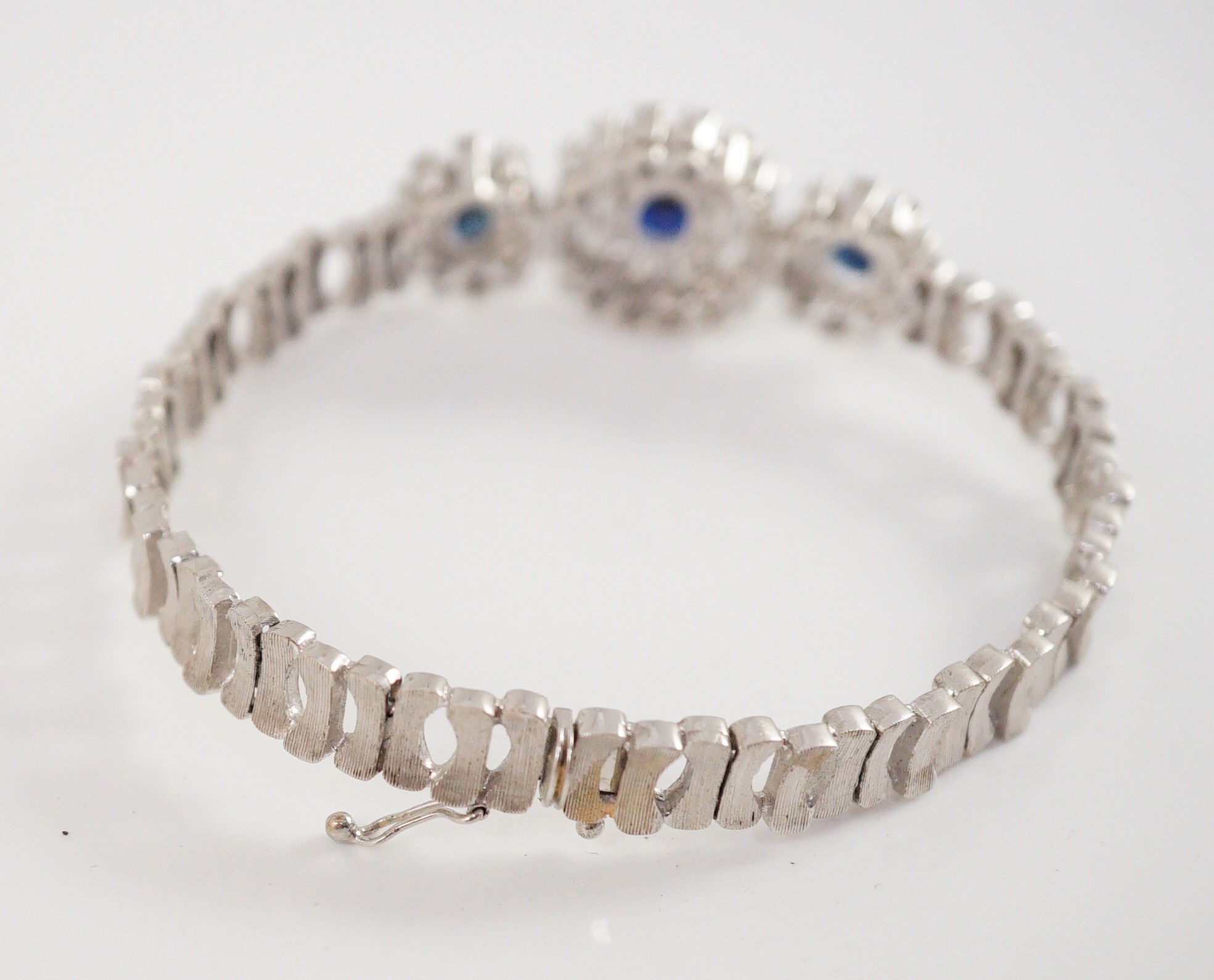 A mid to late 20th century textured 18k white gold, sapphire, round and baguette cut diamond set triple oval cluster bracelet